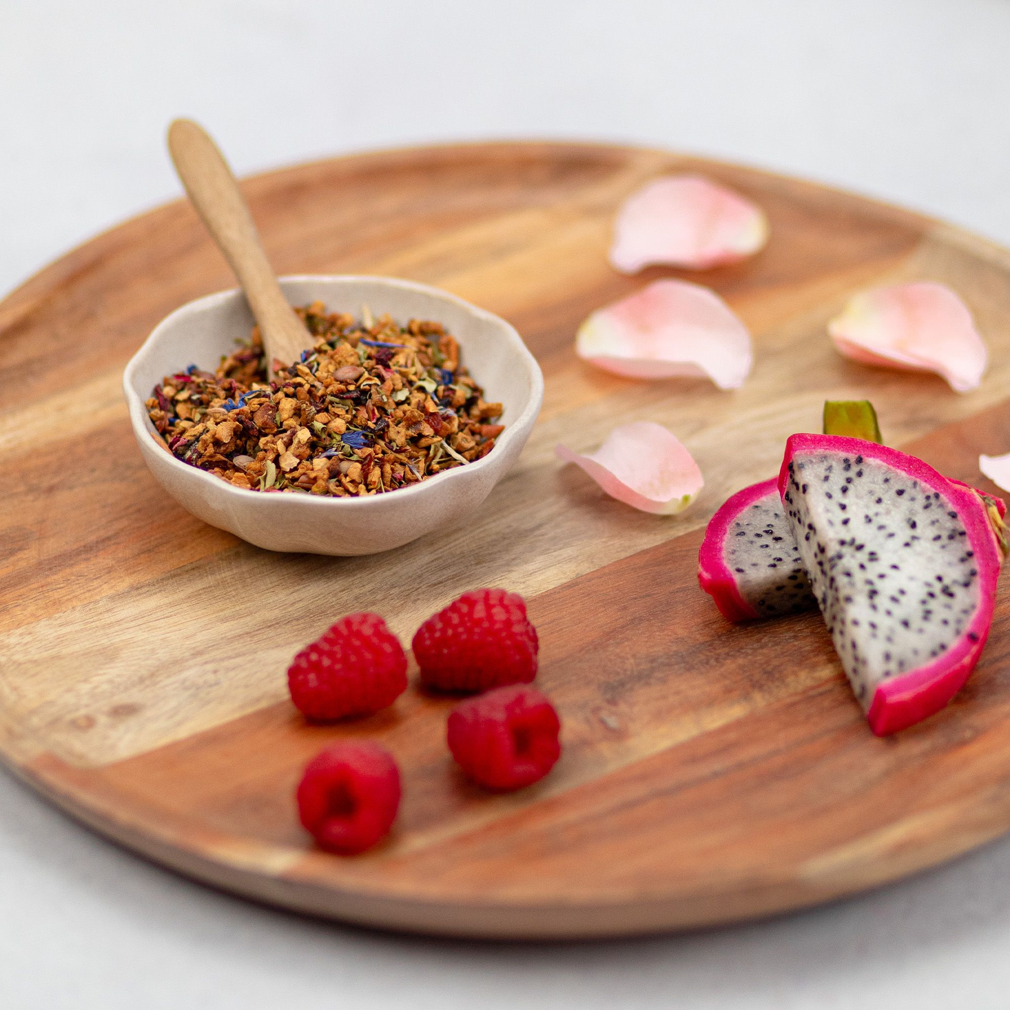 Holztablett mit Schale losem Tee, Himbeeren und Drachenfrucht-Stücken. Rosa Blütenblätter.