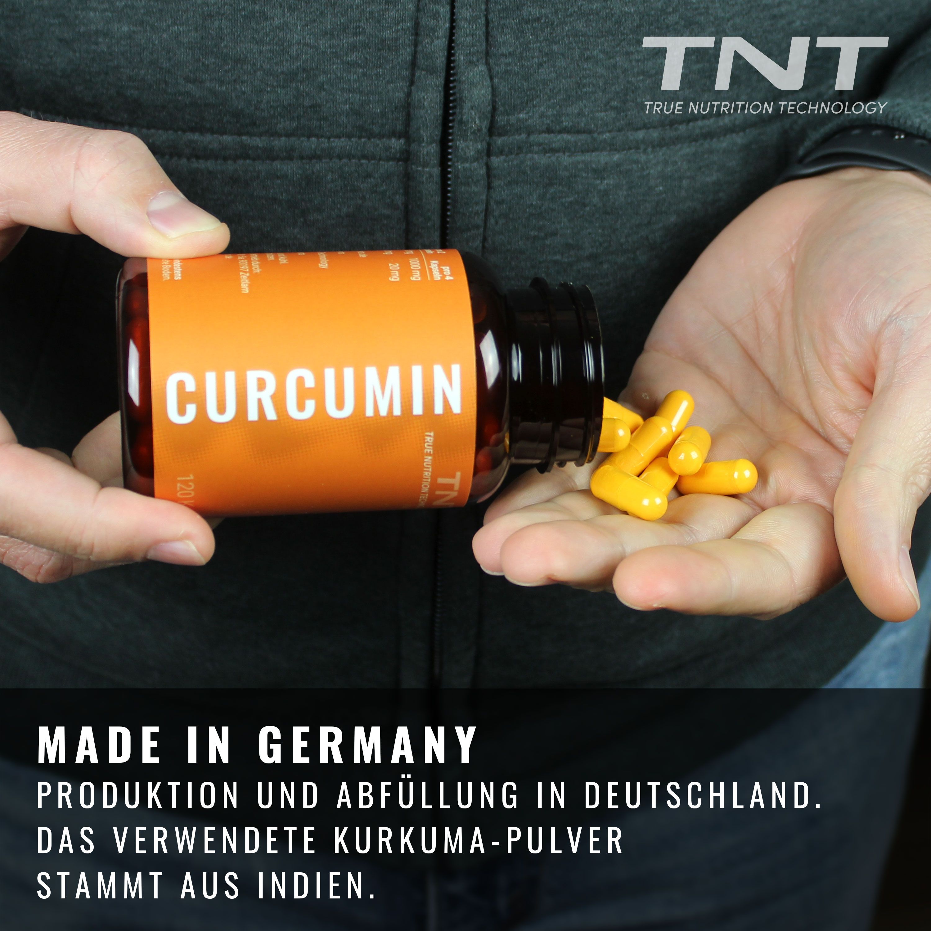 Hände halten eine Kapsel-Dose und schütten Kapseln heraus. Texte: Made in Germany. Produktion und Abfüllung in Deutschland. Kurkuma-Pulver aus Indien.