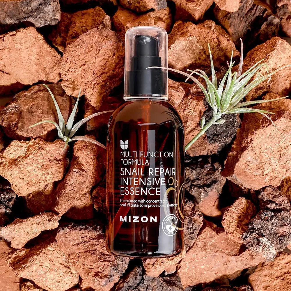 Braune Flasche mit schwarzem Pumpverschluss. Aufschrift: Snail Repair Intensive Essence, MIZON. Auf Steinen und Pflanzen platziert.