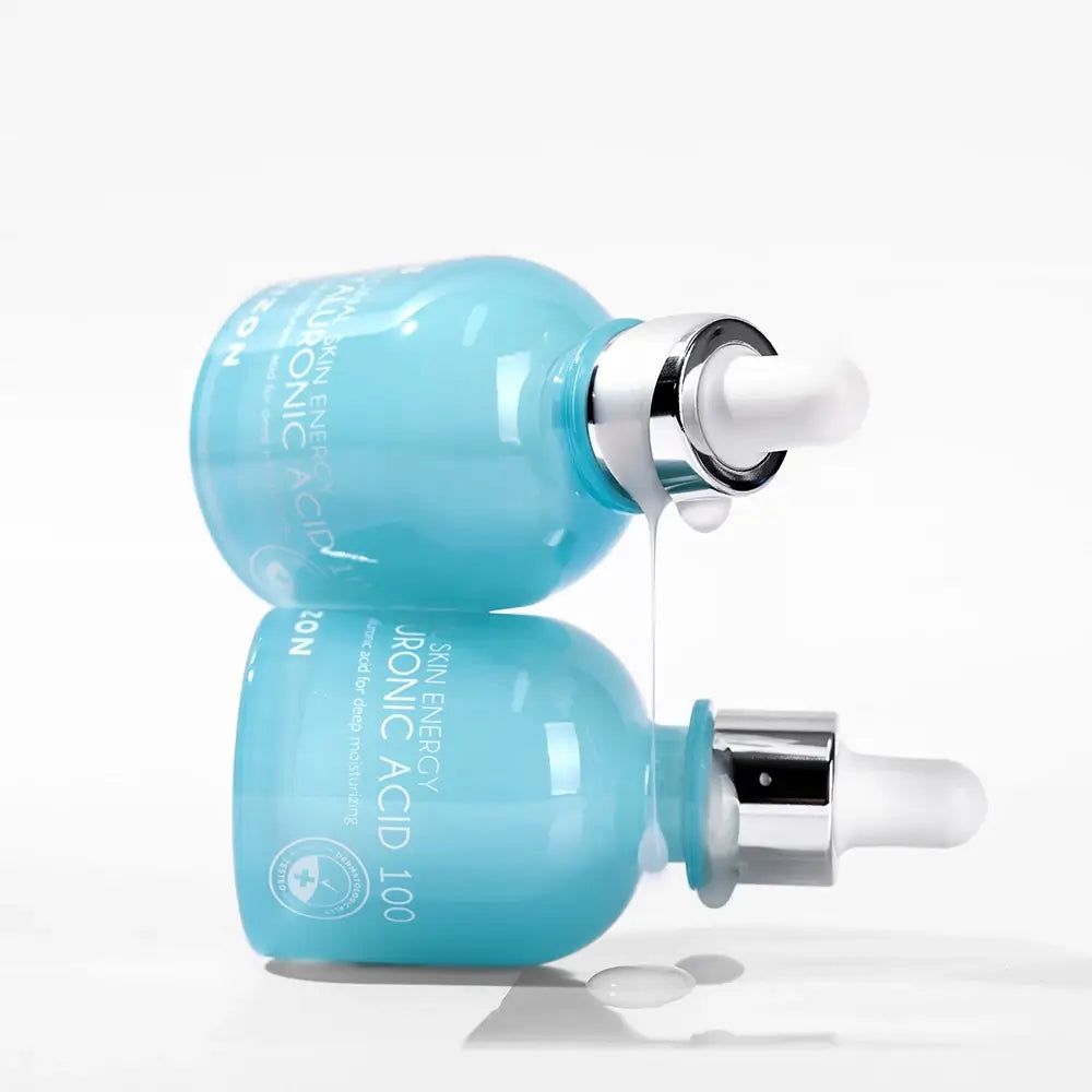 Zwei hellblaue Flaschen mit Pipetten, eine tropft. Aufschrift: Original Skin Energy Hyaluronic Acid 100. Marke: Mizon.
