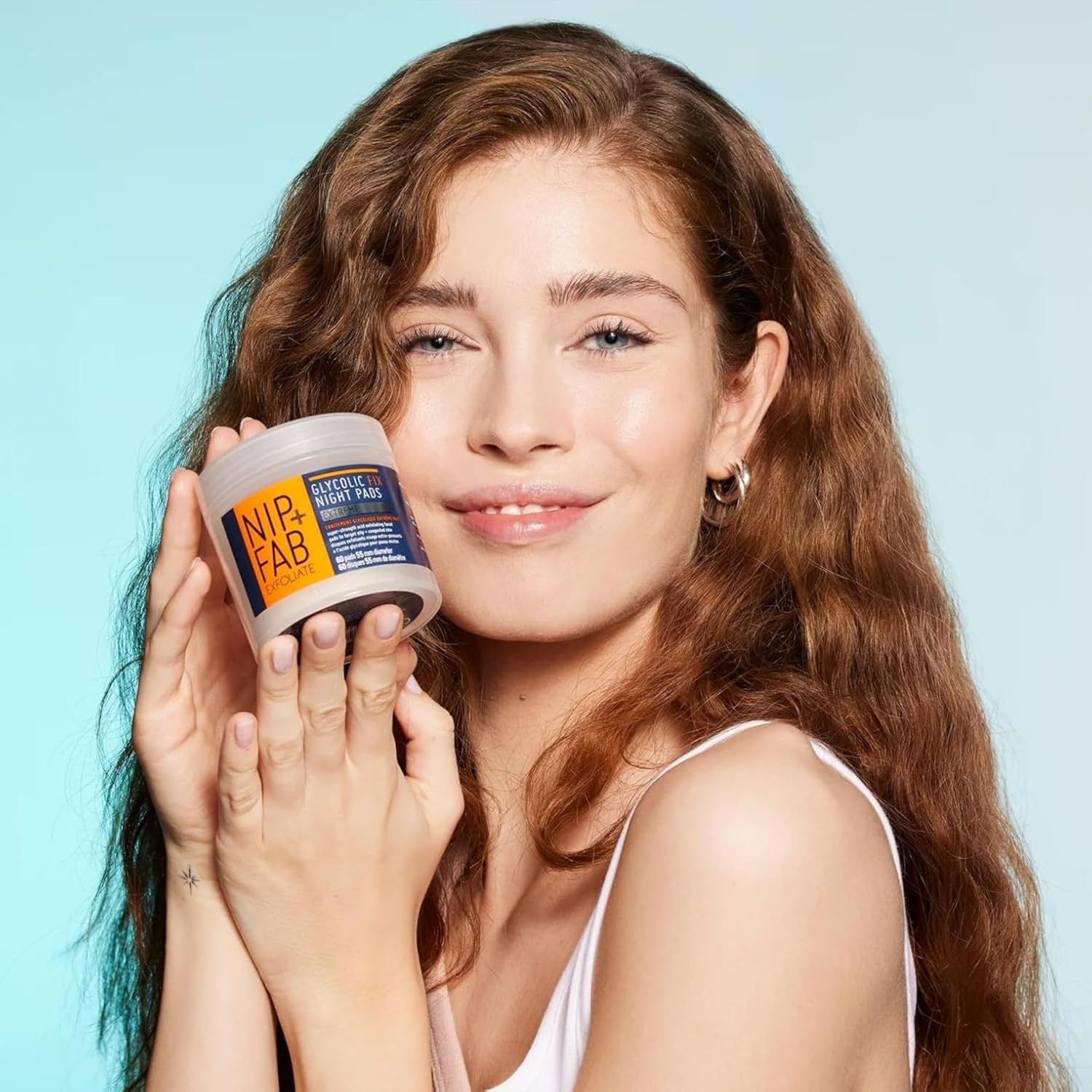 Frau hält ein Tiegel mit NIP+FAB GLYCOLIC FIX NIGHT PADS. Produktverpackung mit Etikett.