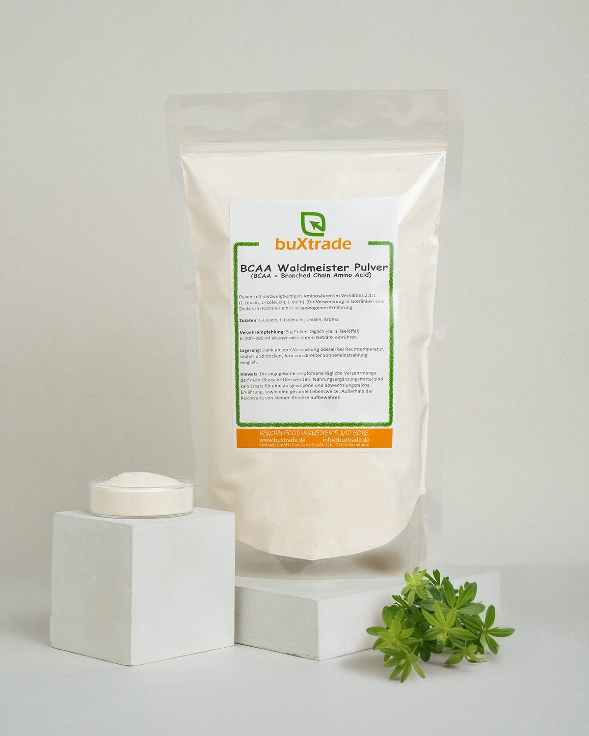 Buxtrade BCAA Waldmeister Pulver in weißem Beutel, daneben ein Messlöffel.