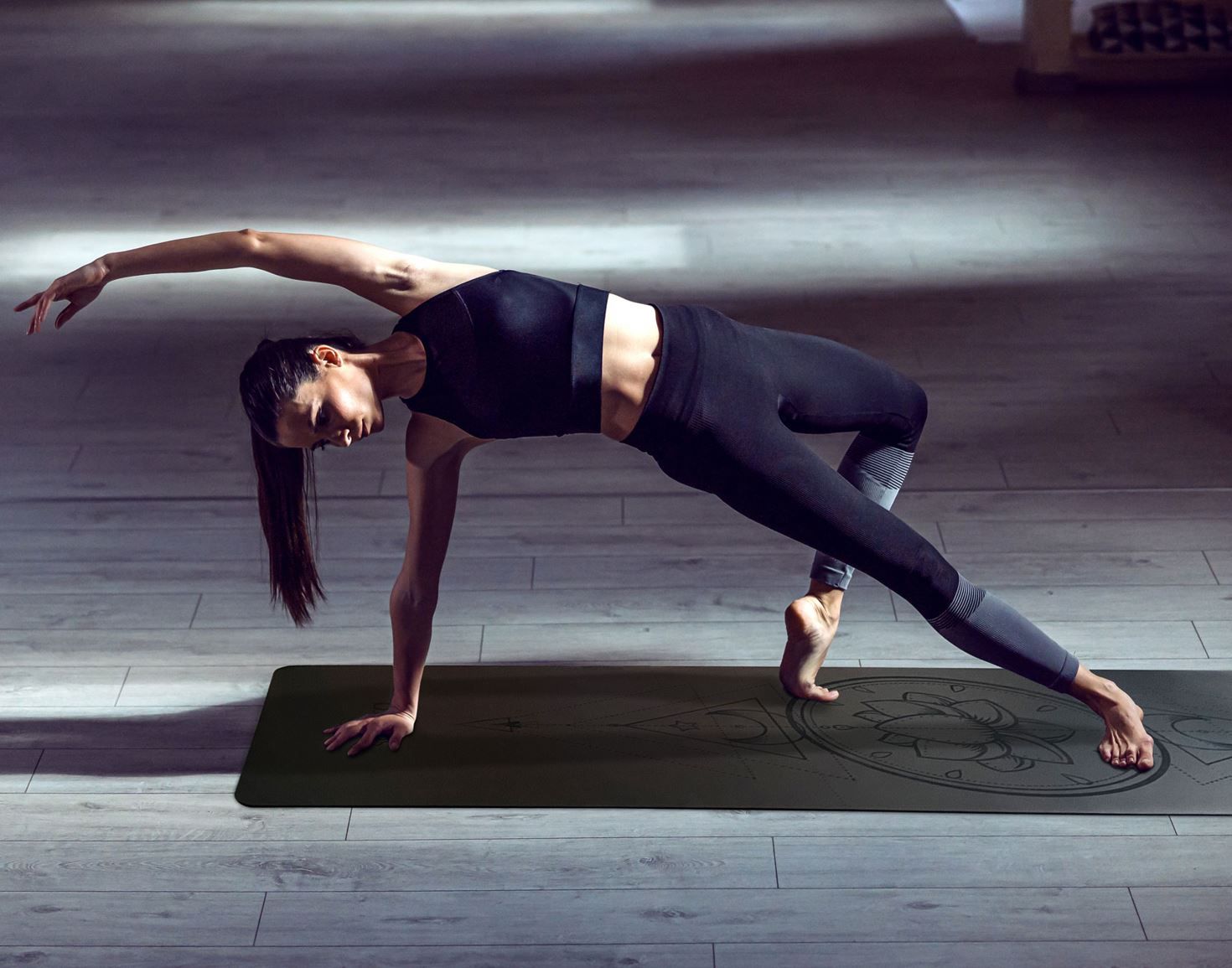 Person praktiziert Yoga auf einer Yogamatte. Die Matte ist dunkelgrau und hat ein Muster.