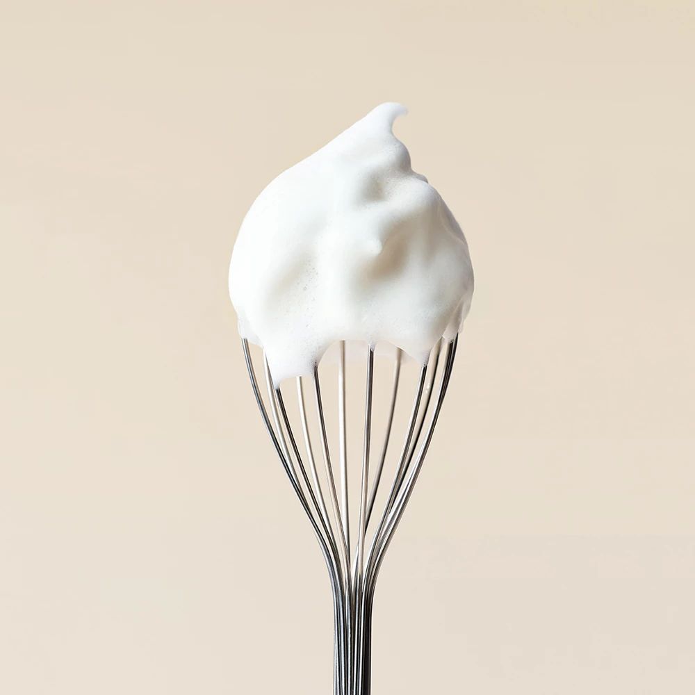 Ein Schneebesen mit einem Klumpen weißen Schaums. Der Schaum ist locker und luftig.