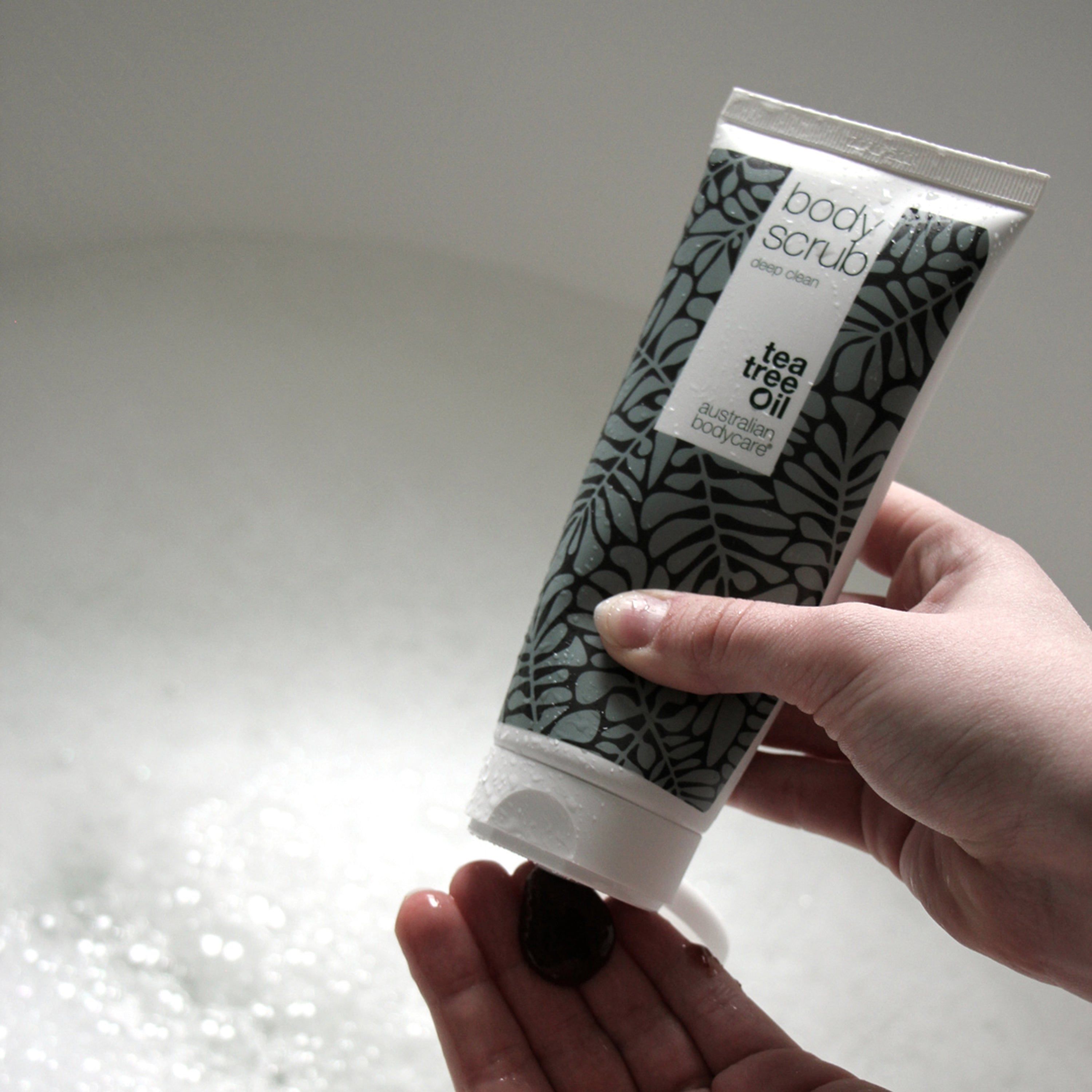 Person drückt Peeling aus Tube. Marke: Australian Bodycare. Text: Tea Tree Oil, Body Scrub, deep clean.