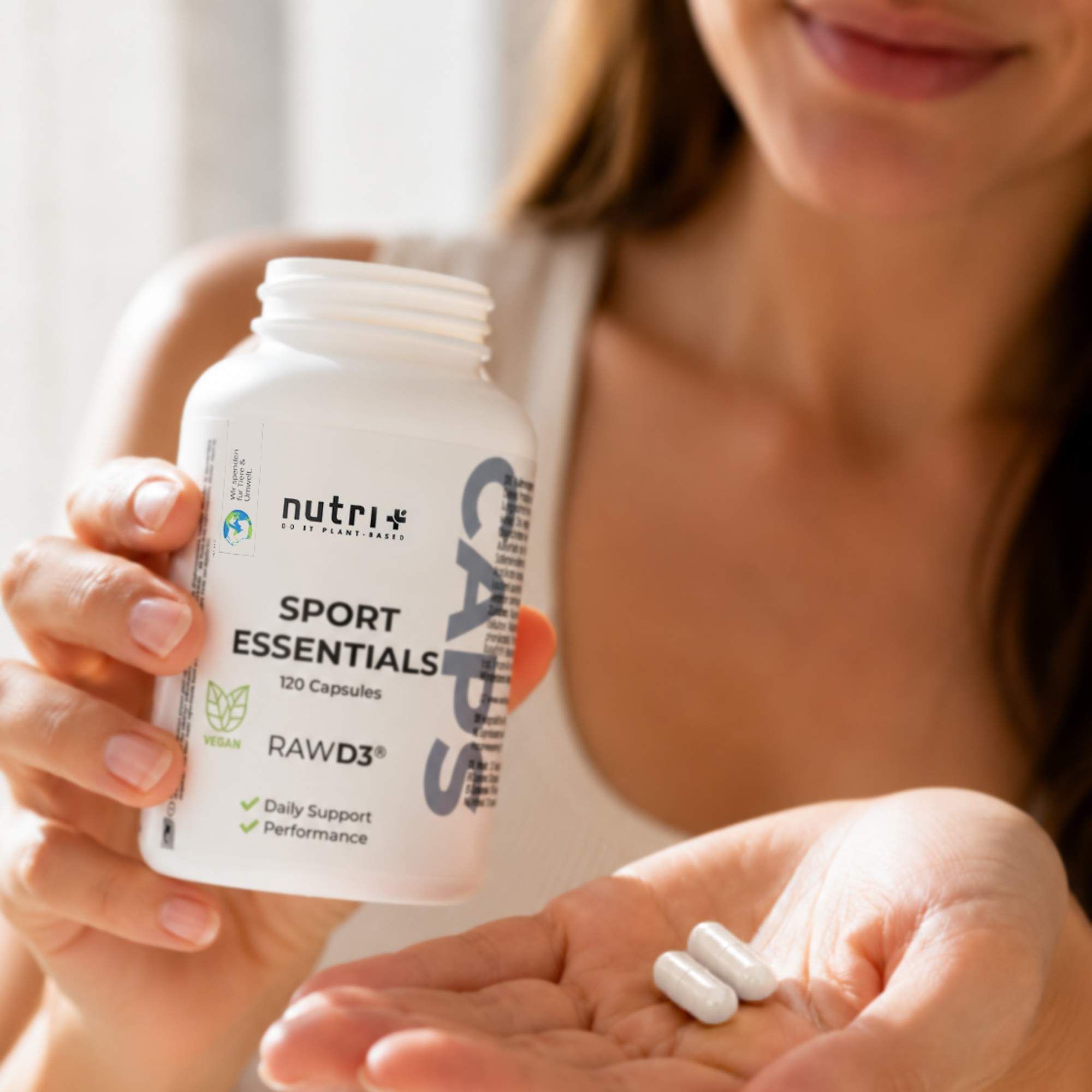 Frau hält Flasche nutri+ Sport Essentials Kapseln und zwei Kapseln in der Hand.