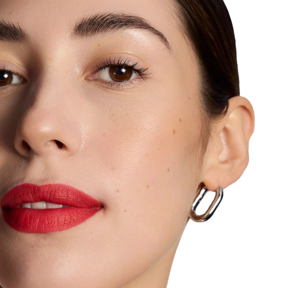 Nahaufnahme eines Gesichts mit rotem Lippenstift. Helle Haut, braune Augen, silberne Ohrringe.