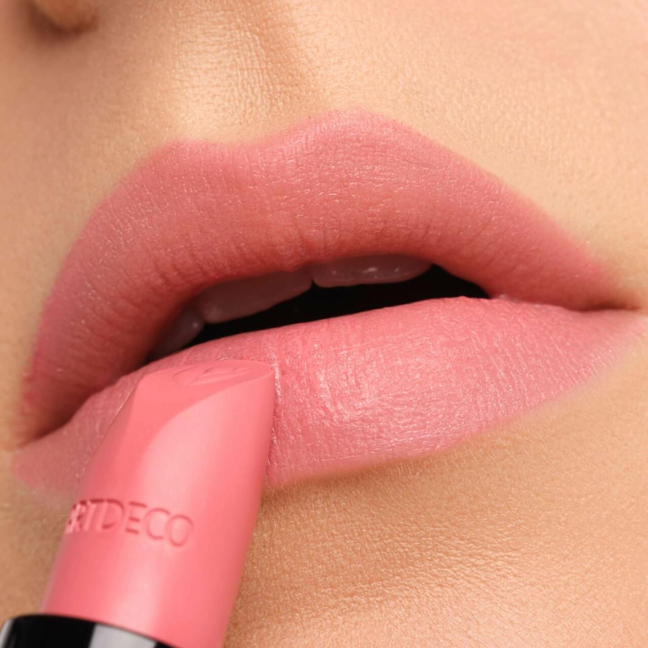 Lippenstift wird auf Lippen aufgetragen. Rosa Lippenstift mit schwarzem Gehäuse. Auf dem Lippenstift steht ARTDECO.