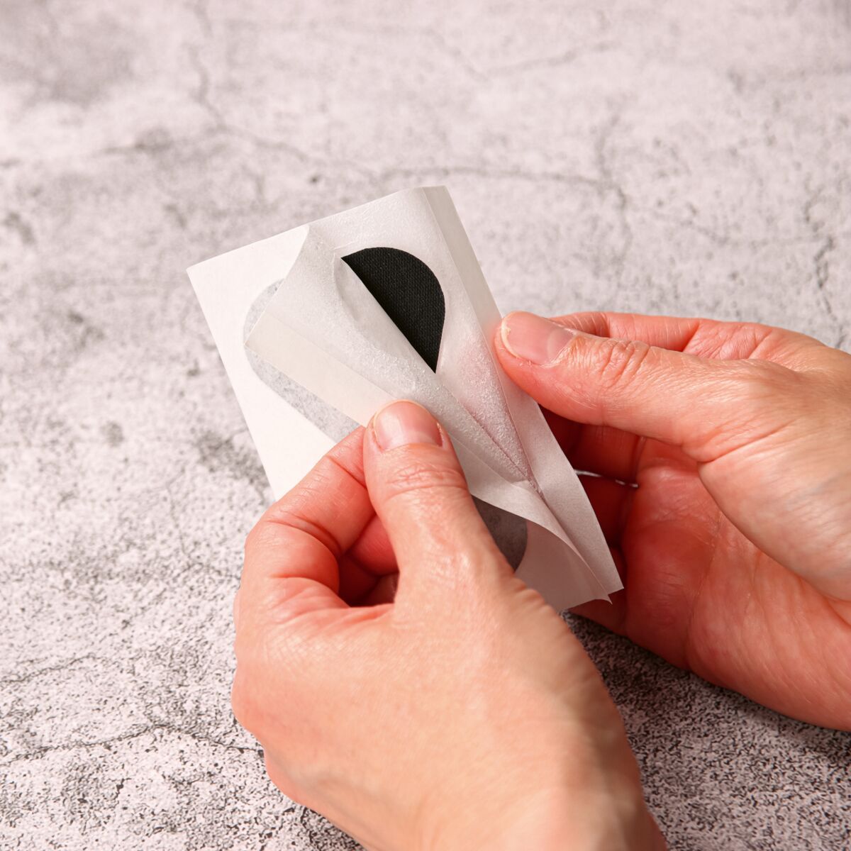Hände lösen schwarzes Fingerkuppenpflaster von Trägerpapier.