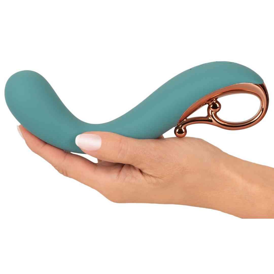 Türkisfarbener Vibrator in einer Hand gehalten. Goldfarbener Ring. Gebogene Form.