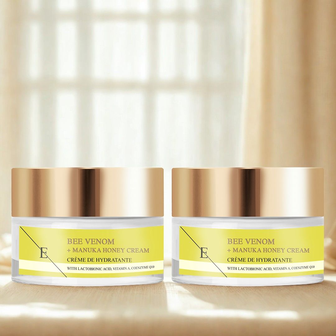 Zwei Creme-Tiegel mit goldfarbenen Deckeln. Gelbe Etiketten mit Text: Bee Venom + Manuka Honey Cream. Auf hellem Hintergrund.