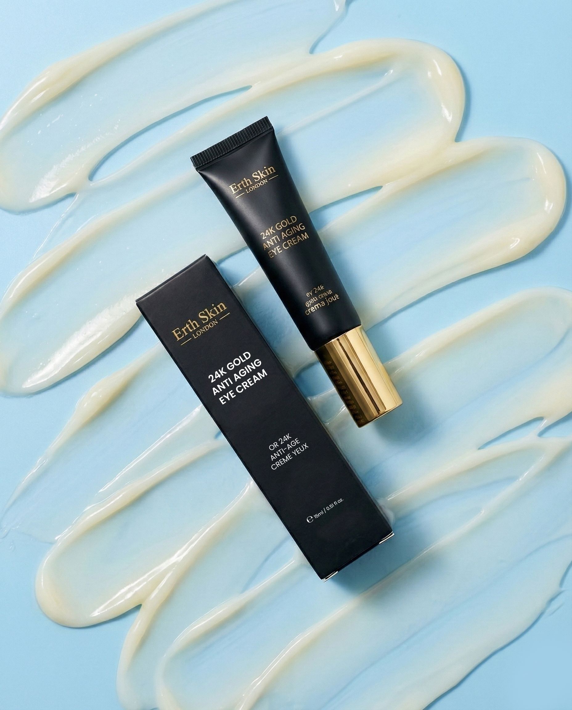 ErthSkin London 24K Gold Augencreme Tube und Faltschachtel, umgeben von cremigen Streifen.