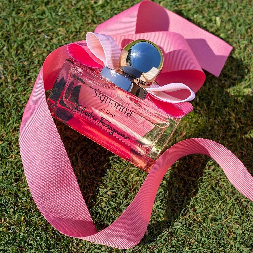 Glasflakon mit rosa Flüssigkeit auf Gras. Goldfarbener Deckel, rosa Schleife. Schriftzug Signorina in fiore und Salvatore Ferragamo.