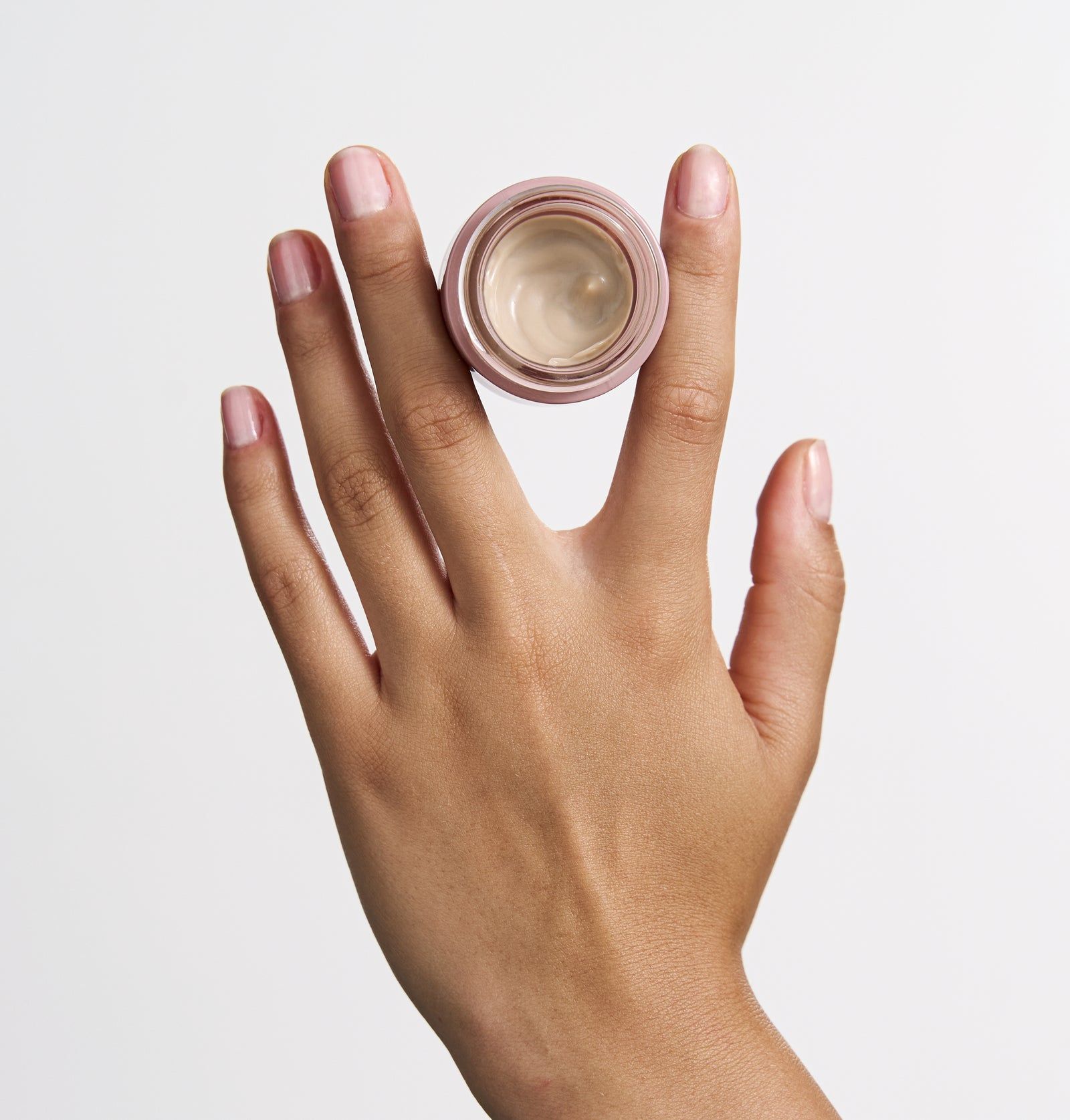 Rosa Dose mit Creme auf einem Finger. Creme hellbeige. Dose mit weißem Deckel. Aufschrift: BB Eye Balm.