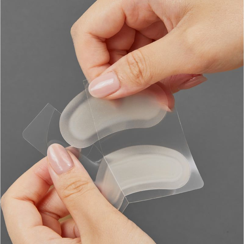 Zwei transparente, ovale Pflaster werden aus einer Verpackung entnommen. Die Pflaster sind in Folie verpackt.