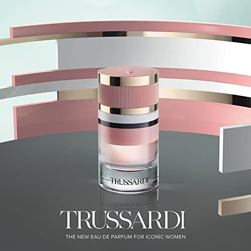 Trussardi Eau de Parfum Flakon auf grauem Untergrund mit abstrakten rosa und silbernen Elementen.