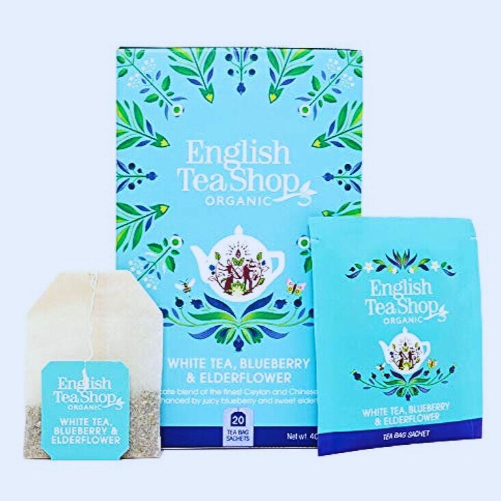 Hellblaue Teebox, Teebeutel und einzelnes Teebeutel-Sachet. Aufschrift: Weißer Tee, Blaubeere & Holunderblüte. 20 Teebeutel.