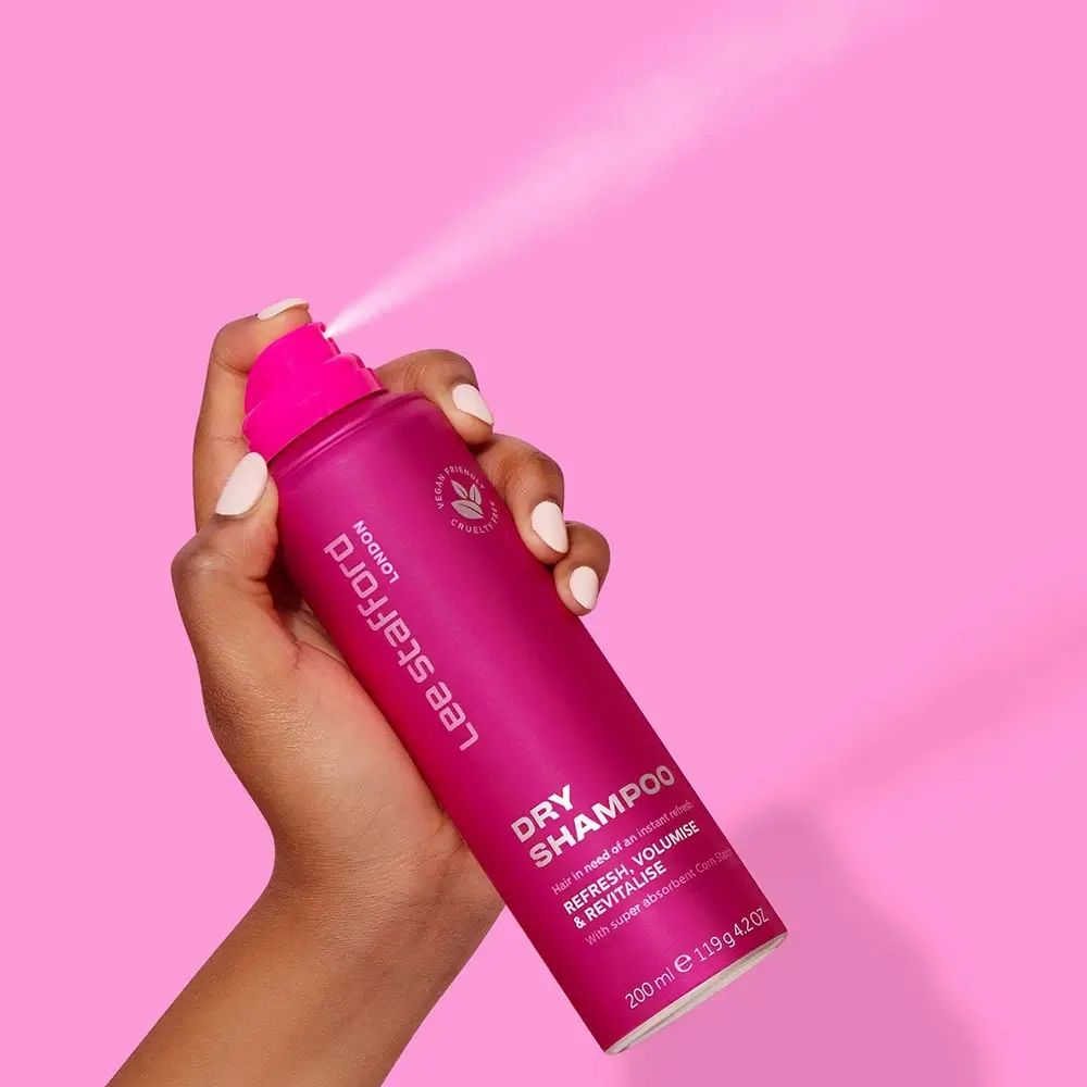 Hand hält rosa Trockenshampoo-Dose. Sprühnebel. Aufschrift: LEE STAFFORD LONDON, DRY SHAMPOO, REFRESH, VOLUMISE & REVITALISE.