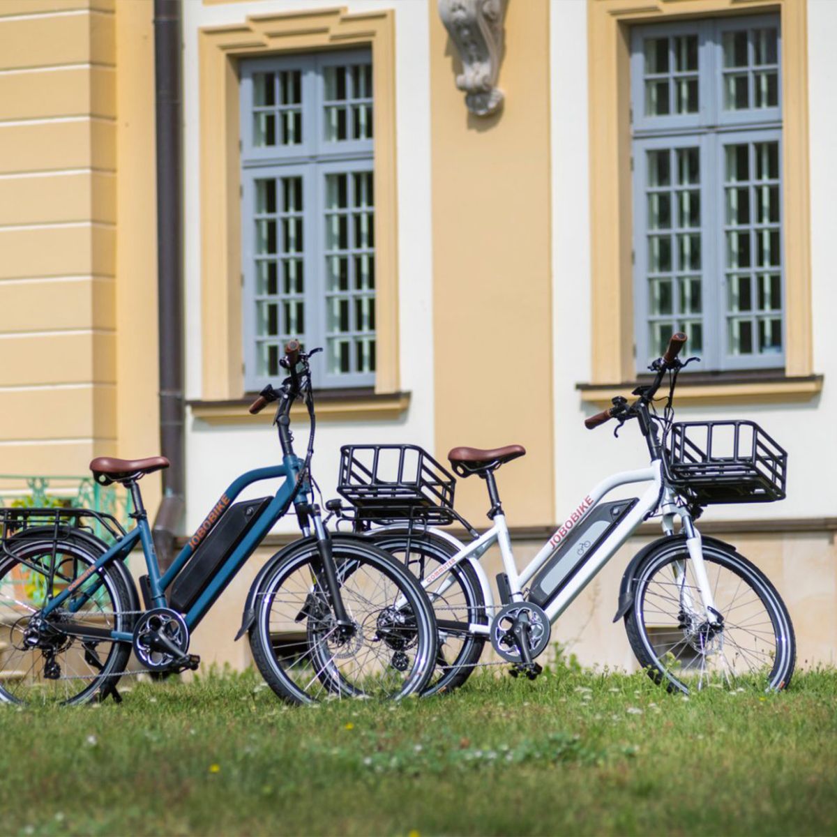 Drei E-Bikes, blau, schwarz und weiß. Körbe vorne, Akkus am Rahmen. JOBOBIKE-Logo sichtbar.