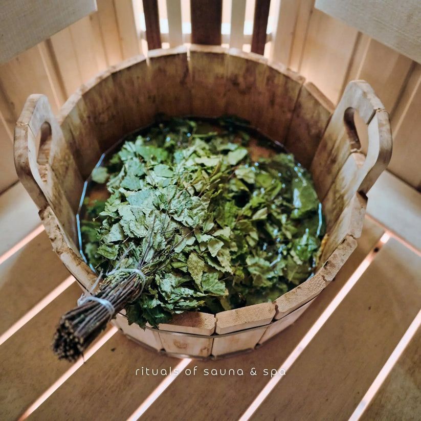 Bündel Birkenreisig in einem Holzeimer mit Wasser. Text: Rituals of sauna & spa.