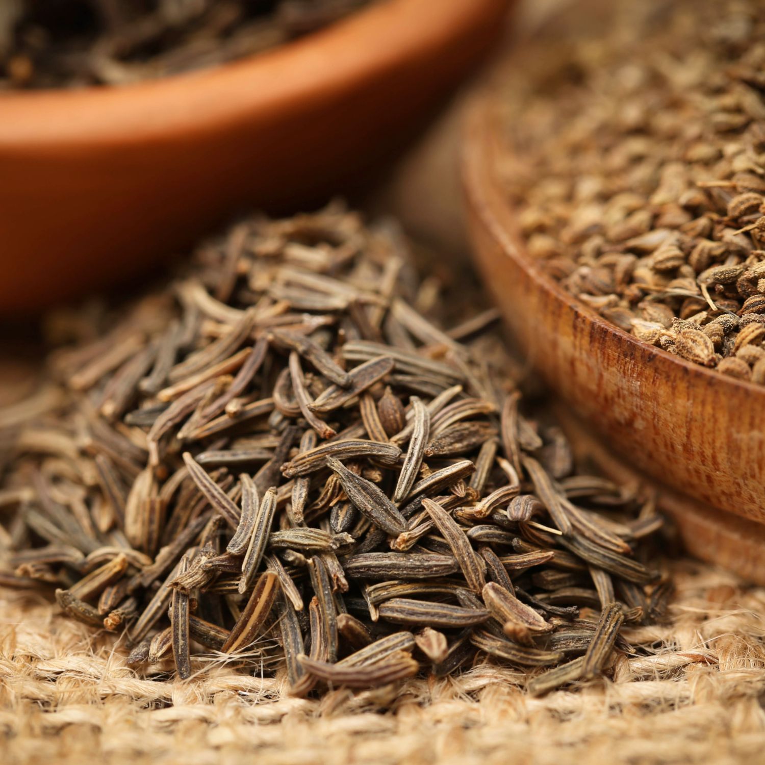 Kümmelsamen auf grobem Stoff. Im Hintergrund Holzschalen mit Samen.