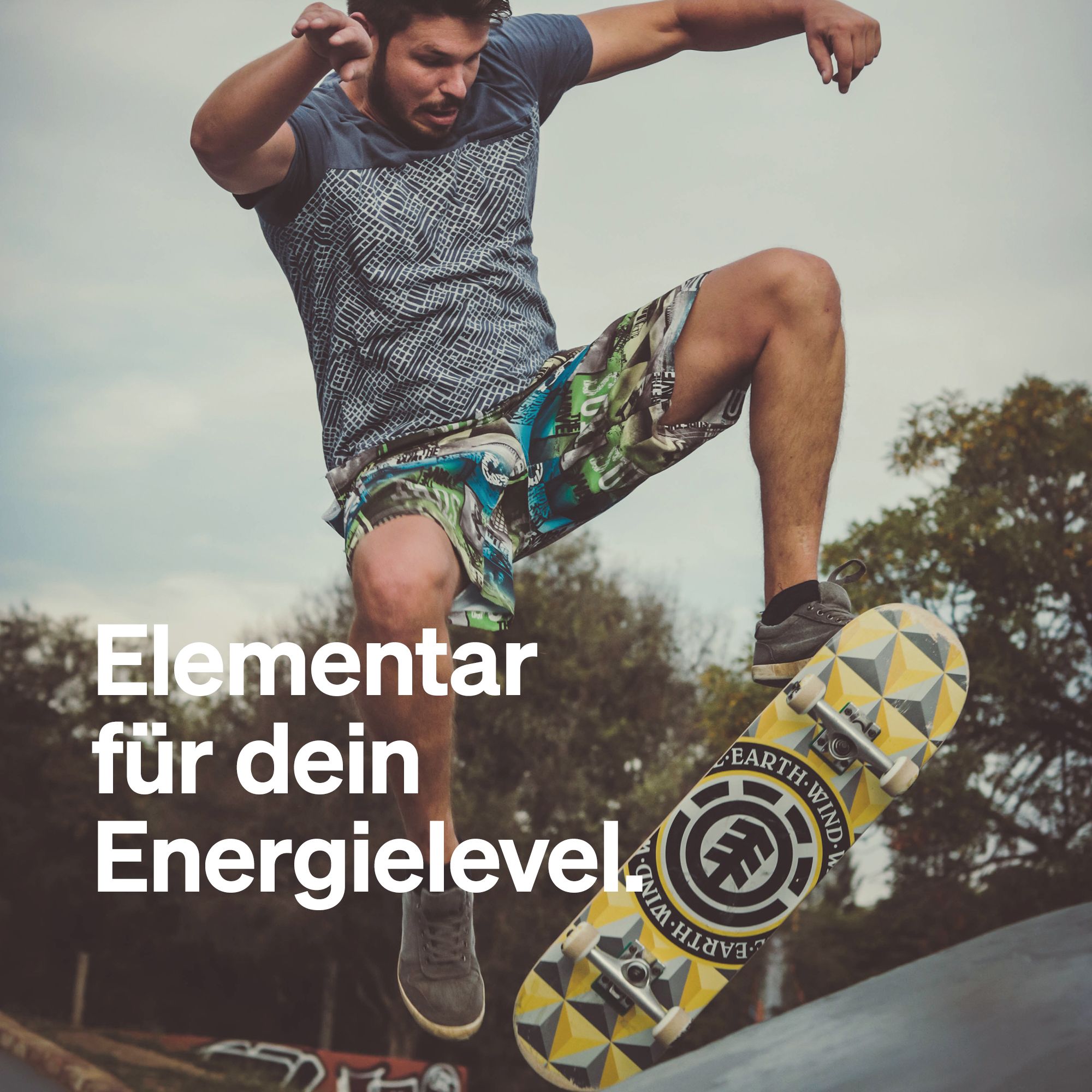 Skateboarder in Aktion. Aufschrift: Elementar für dein Energielevel. Skateboard mit Logo.
