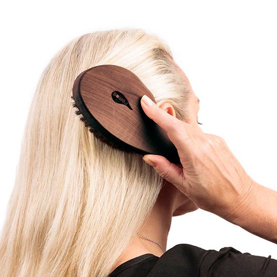 Holzhaarbürste mit Wildschweinborsten wird in blondes Haar gekämmt.