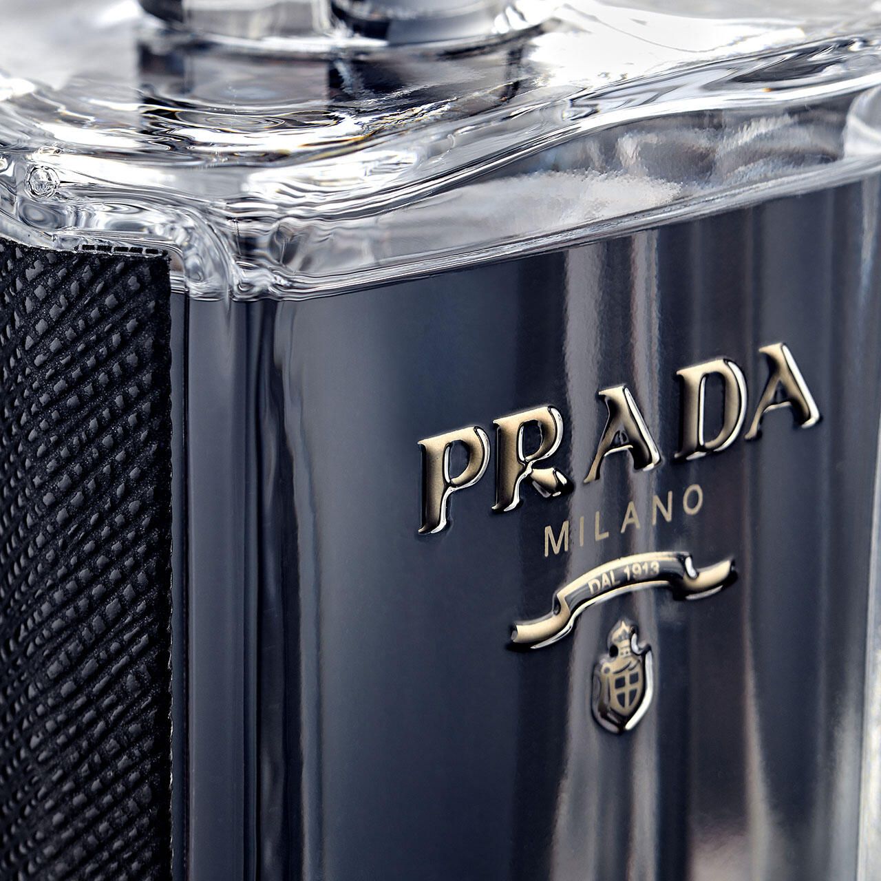 Nahaufnahme des Prada-Logos auf einem Flakon. Goldfarbener Schriftzug Prada Milano. Kleines Wappen darunter.
