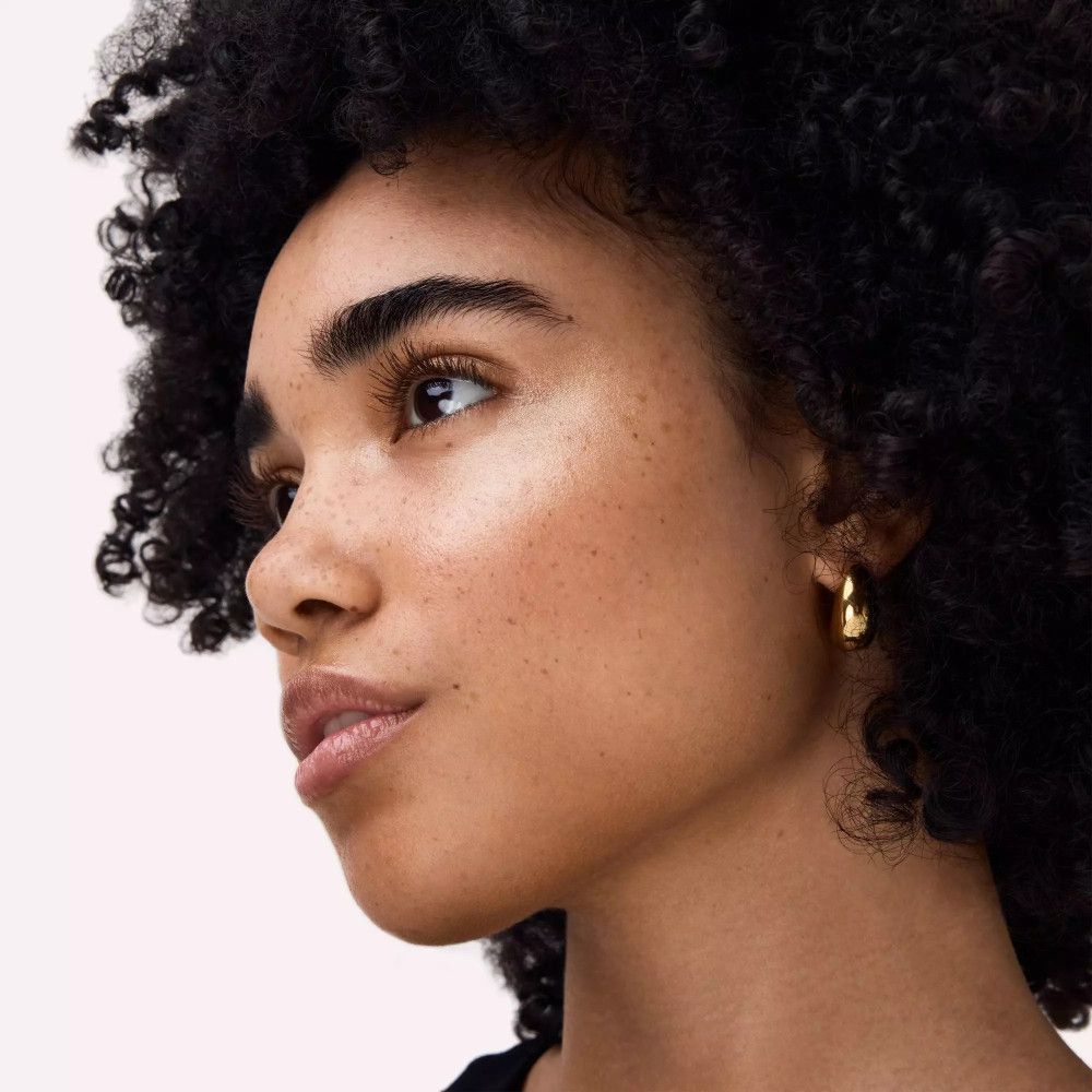 Porträt einer Frau mit Sommersprossen und goldenen Creolen. Hautton: hellbraun.