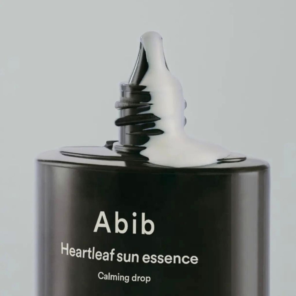 Nahaufnahme einer schwarzen Flasche, aus der eine weiße Creme austritt. Aufschrift: Abib Heartleaf Sun Essence.