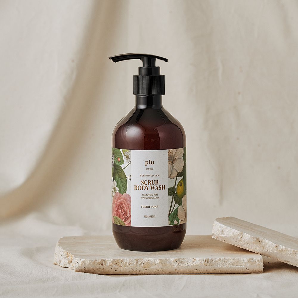 Braune Flasche mit Pumpe. Aufkleber mit floralem Design und Text: SCRUB BODY WASH, FLEUR SOAP. Marke: plu. Auf Stein platziert.