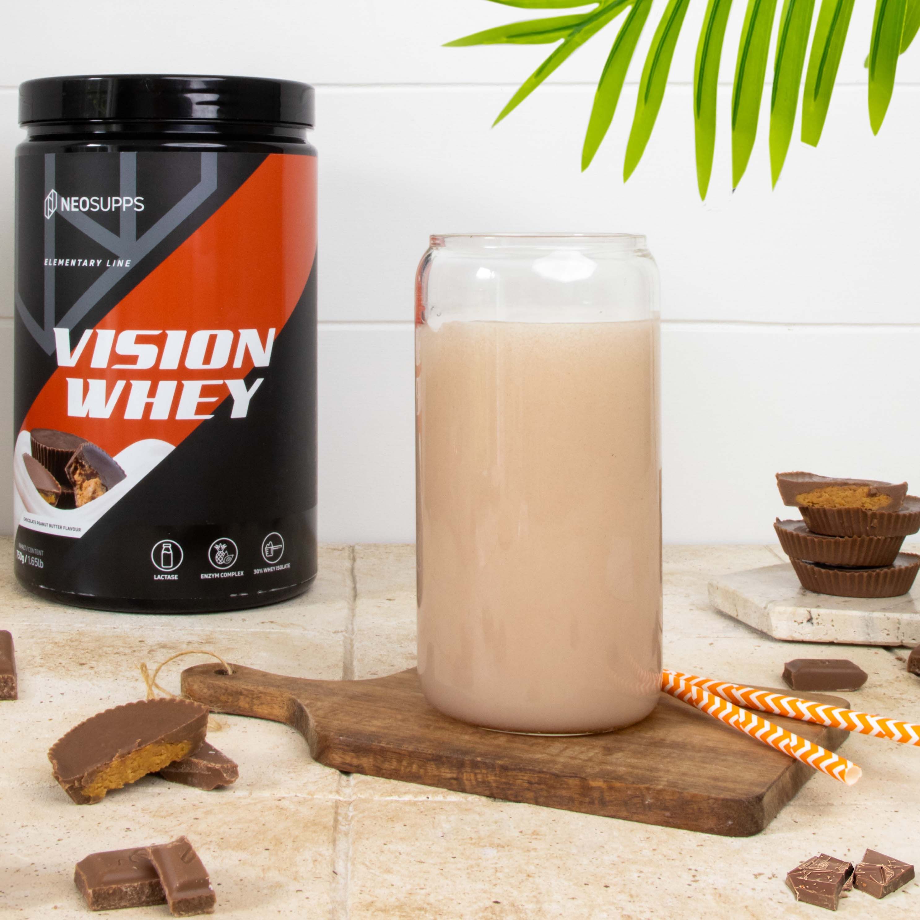 Produkt-Dose neben Glas mit Getränk. Aufschrift: Vision Whey. Auf Holzbrettchen: Schoko-Erdnussbutter-Happen und Trinkhalme.