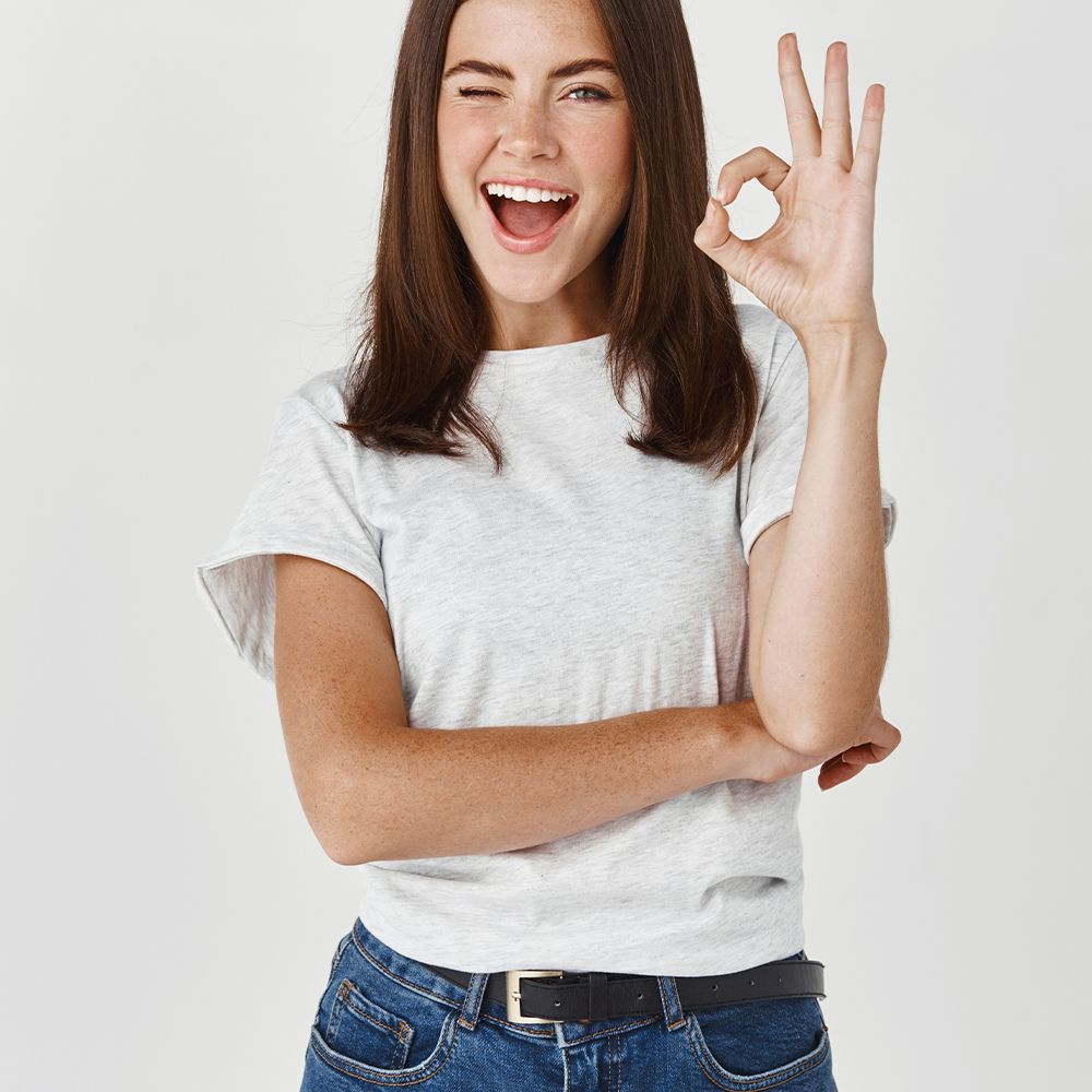Eine junge Frau zwinkert und zeigt ein OK-Zeichen mit der Hand.