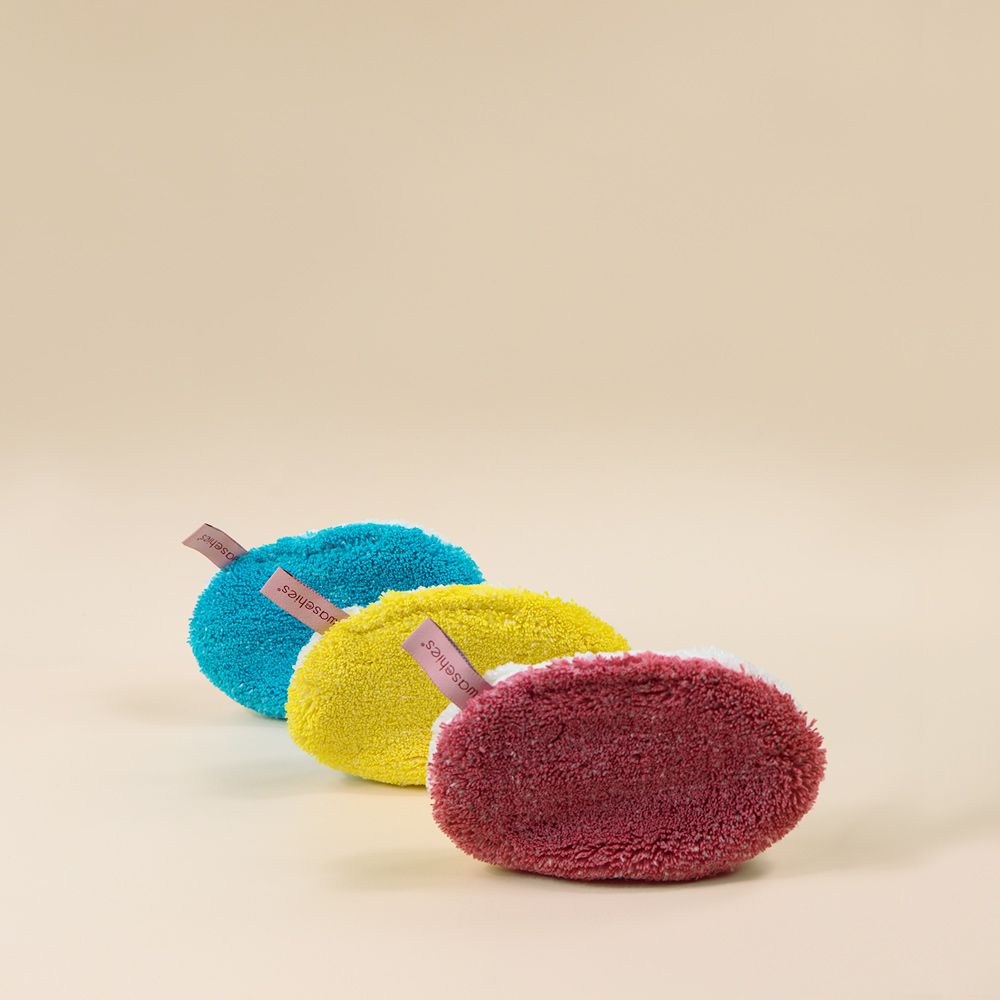 Drei farbige Waschpads nebeneinander. Die Pads sind blau, gelb und rosa. An jedem Pad ist ein kleines Etikett mit dem Logo "waschies" befestigt.