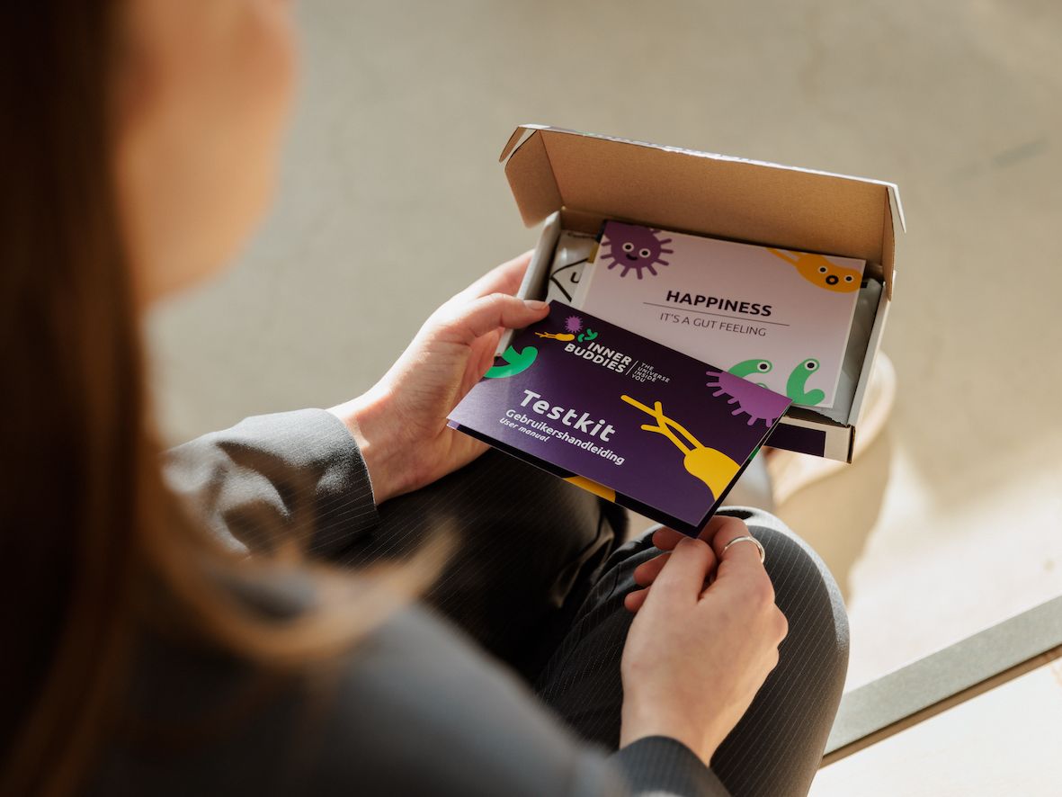 Person hält eine Karte mit Aufschrift Testkit und eine weitere Karte mit dem Logo Inner Buddies. Geöffneter Karton im Hintergrund.