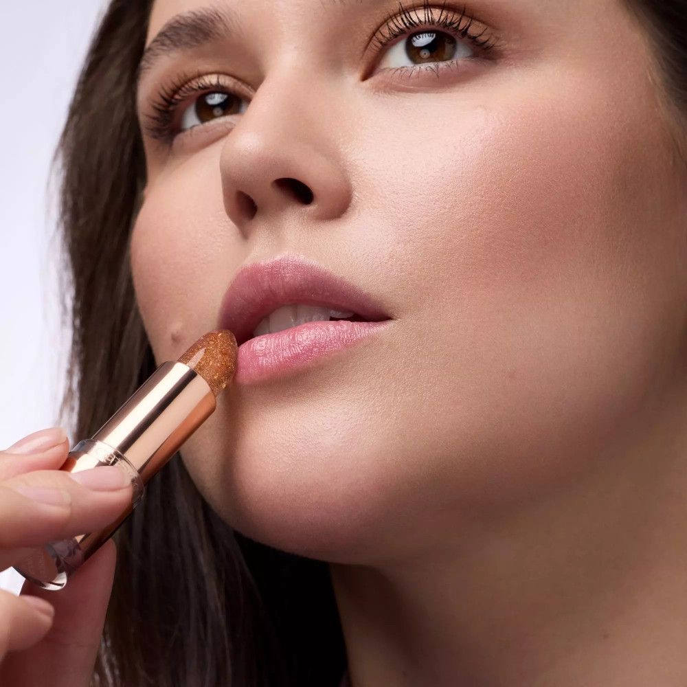 Frau trägt Lippenbalsam auf. Roségoldene Hülse. Lippen sind leicht glänzend.