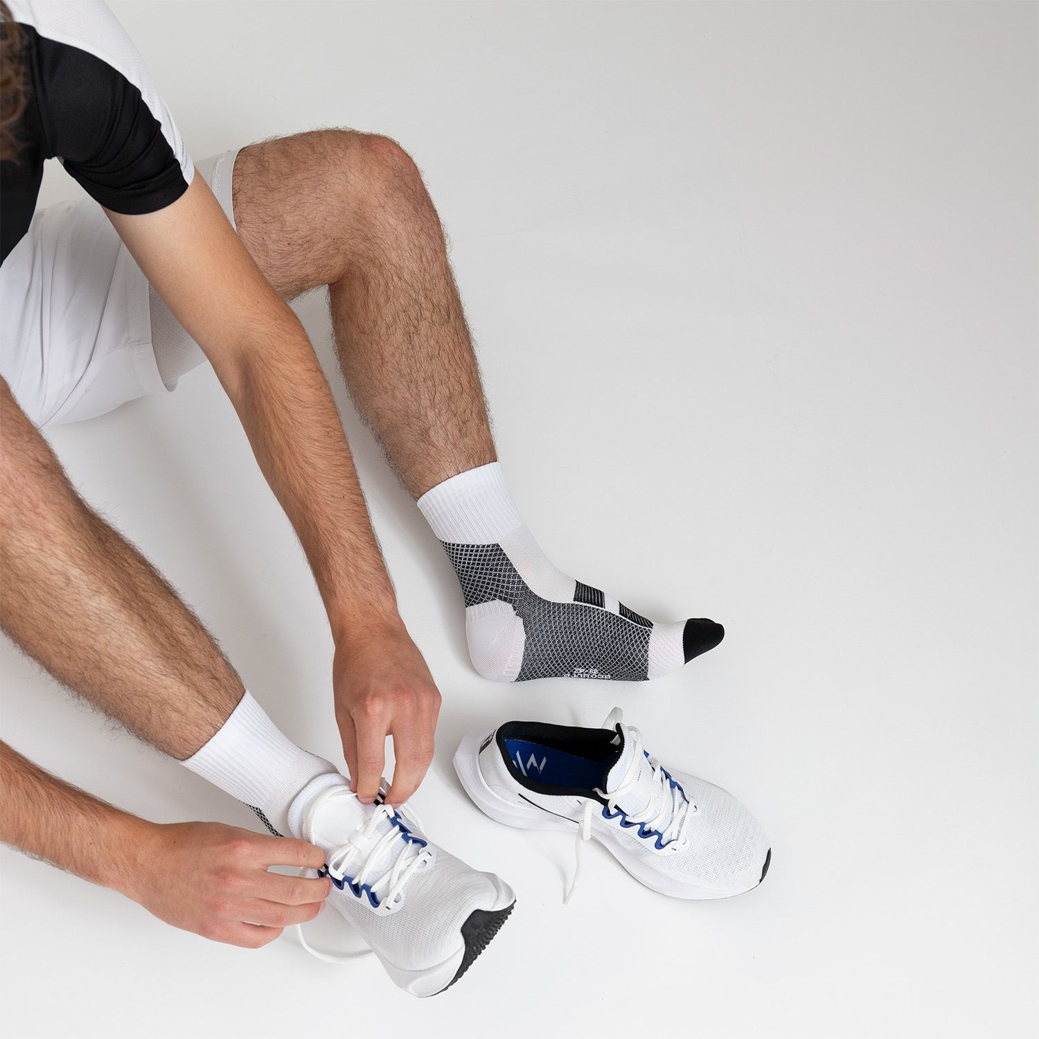 Person bindet Schnürsenkel an weißen Sportschuhen. Eine Socke liegt daneben. Socken sind weiß mit grauen Akzenten.