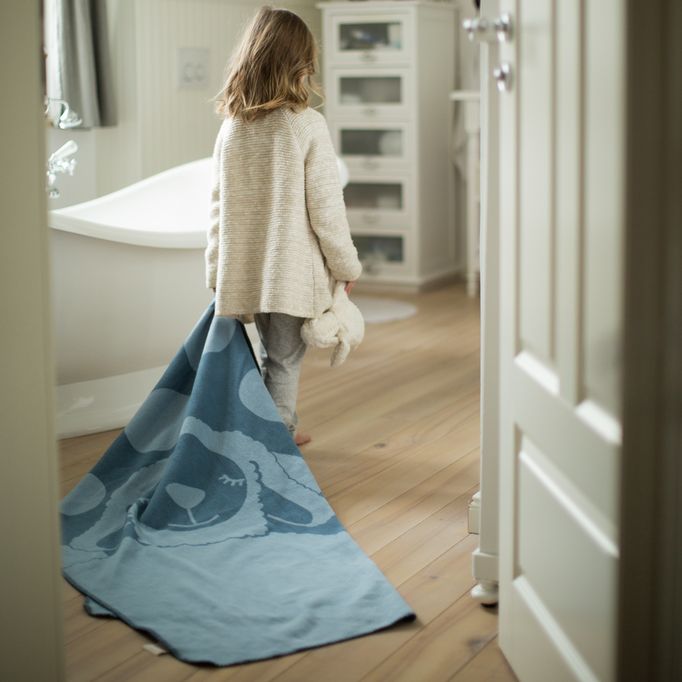 Kind mit blauem Schaf-Plaid in der Hand, geht durch eine Tür. Badezimmer im Hintergrund.