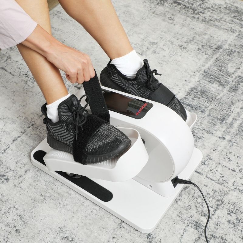 Nahaufnahme: Füße in schwarzen Schuhen auf Mini-Ellipsentrainer. Schwarze Riemen. Person befestigt Riemen.