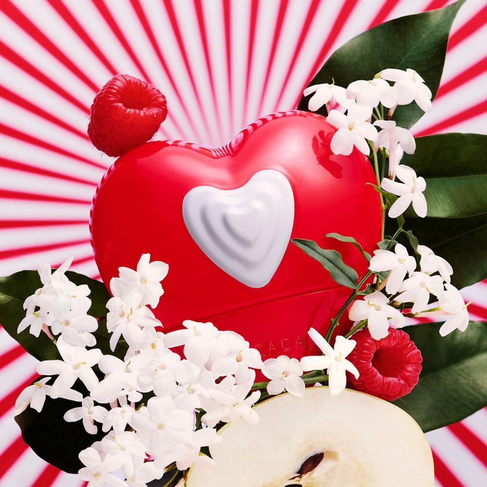 Roter Herzflakon mit weißem Herz. Dekoriert mit Jasminblüten, Himbeeren und Birnenscheibe. Hintergrund mit roten Streifen.