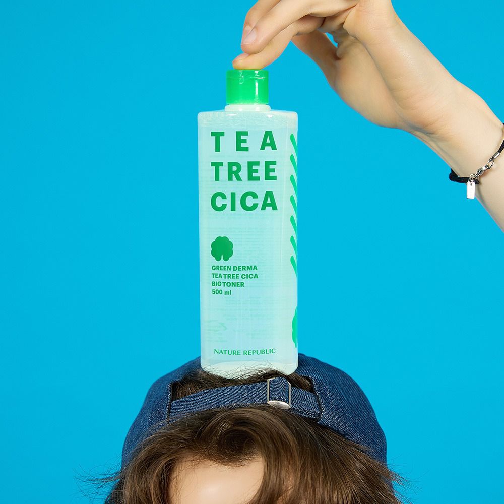 Produktflasche auf dem Kopf einer Person. Aufschrift: TEA TREE CICA, GREEN DERMA, BIG TONER. Grüner Deckel.