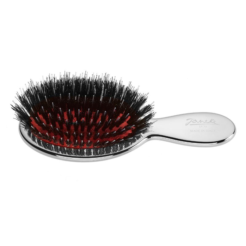 Kleine, ovale Haarbürste mit silberfarbenem Griff. Schwarze Borsten auf rotem Untergrund. Marke Janeke, Made in Italy.