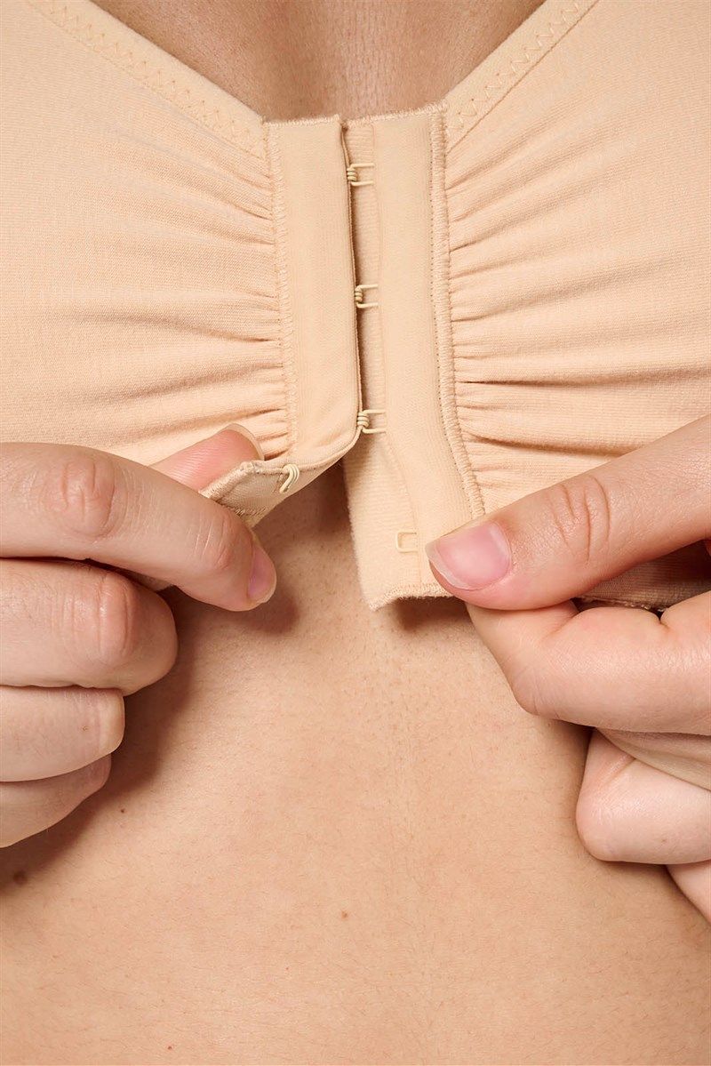 Nahaufnahme des Frontverschlusses eines beigefarbenen BHs. Hände öffnen den Verschluss.