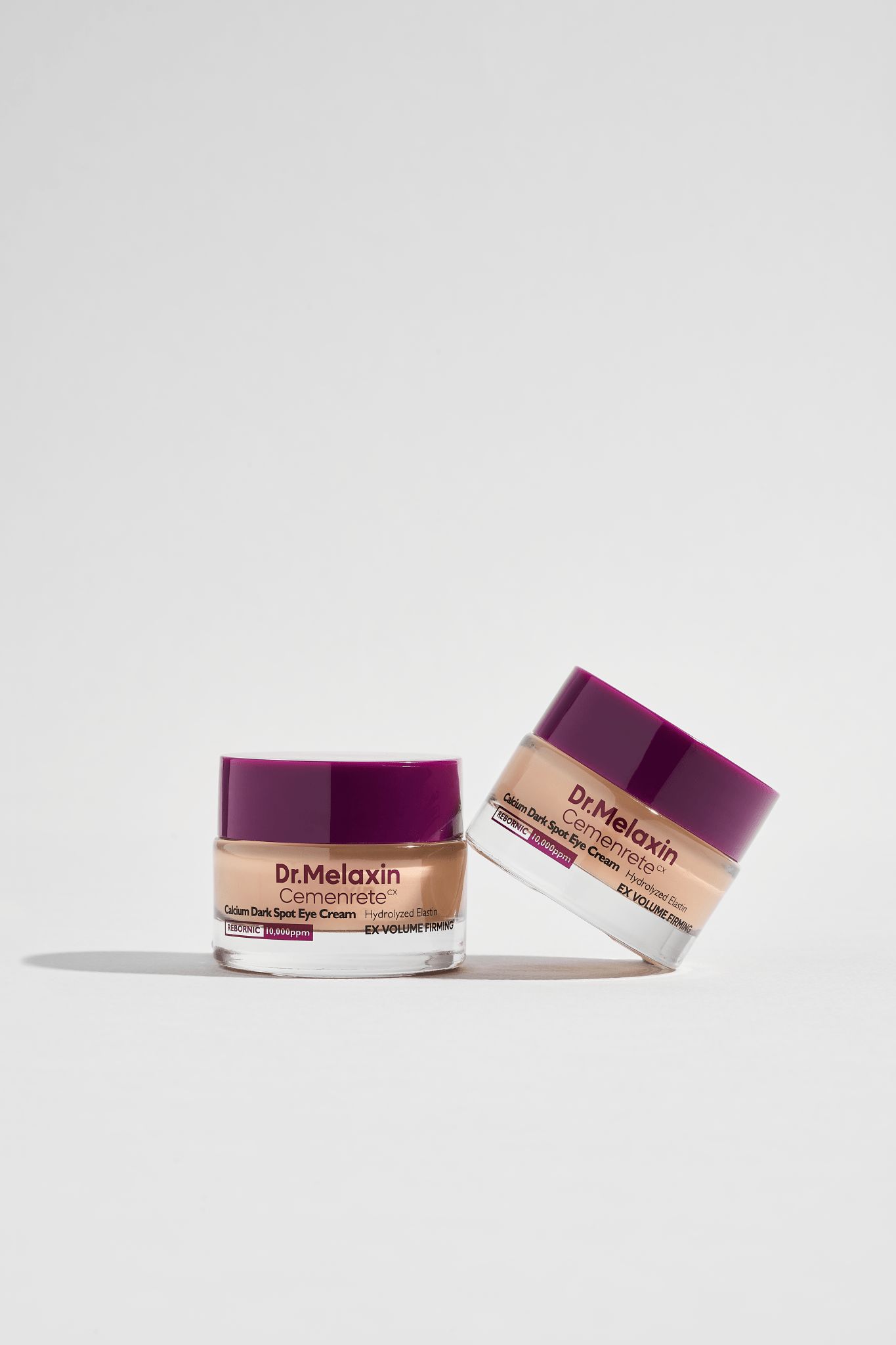 Zwei Tiegel Dr.Melaxin Cemenrete Calcium Dark Spot Eye Cream. Lila Deckel, beige Creme. Weißer Hintergrund.