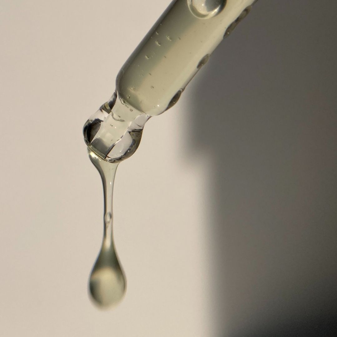 Nahaufnahme einer Pipette mit tropfendem Öl. Klare Flüssigkeit tropft aus der Pipette.