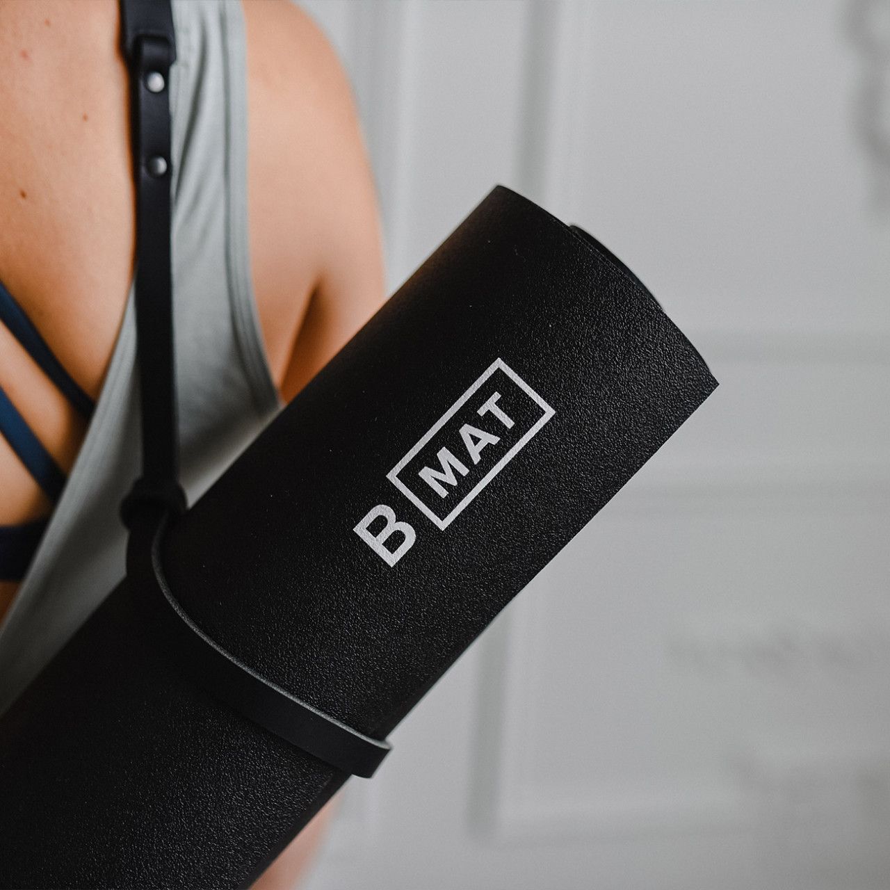 Gerollte schwarze Yogamatte mit Trageriemen. Logo "B MAT" ist sichtbar.