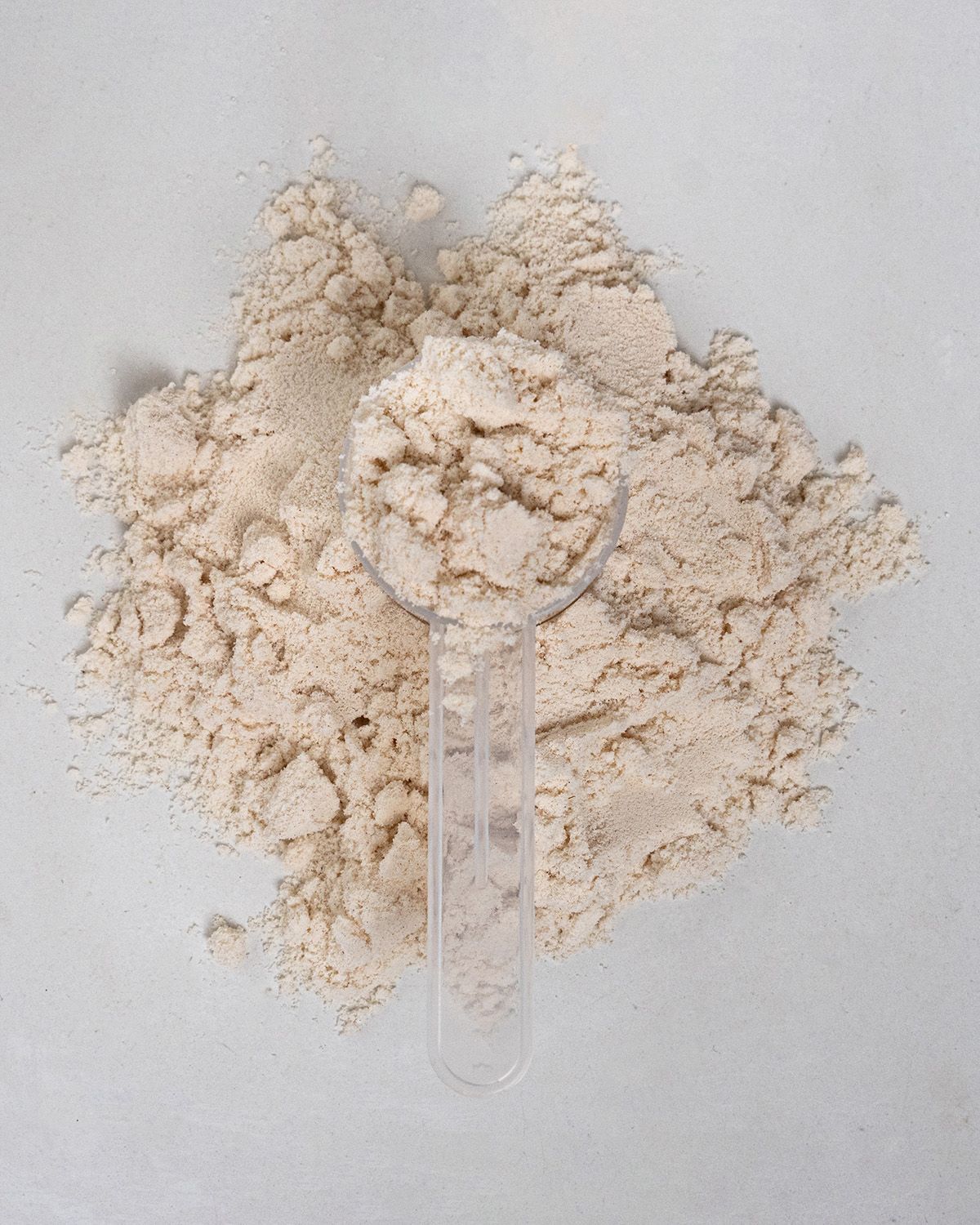Messlöffel mit Proteinpulver. Pulver liegt verstreut. Auf weißem Untergrund.