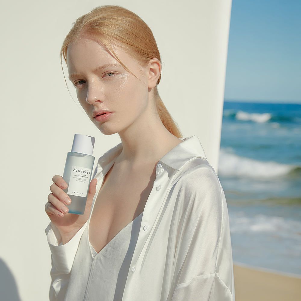 Frau hält eine blaue Flasche mit weißem Deckel. Aufkleber mit Text: CENTELLA, HYALU-CICA, BRIGHTENING TONER. Marke: SKIN1004.