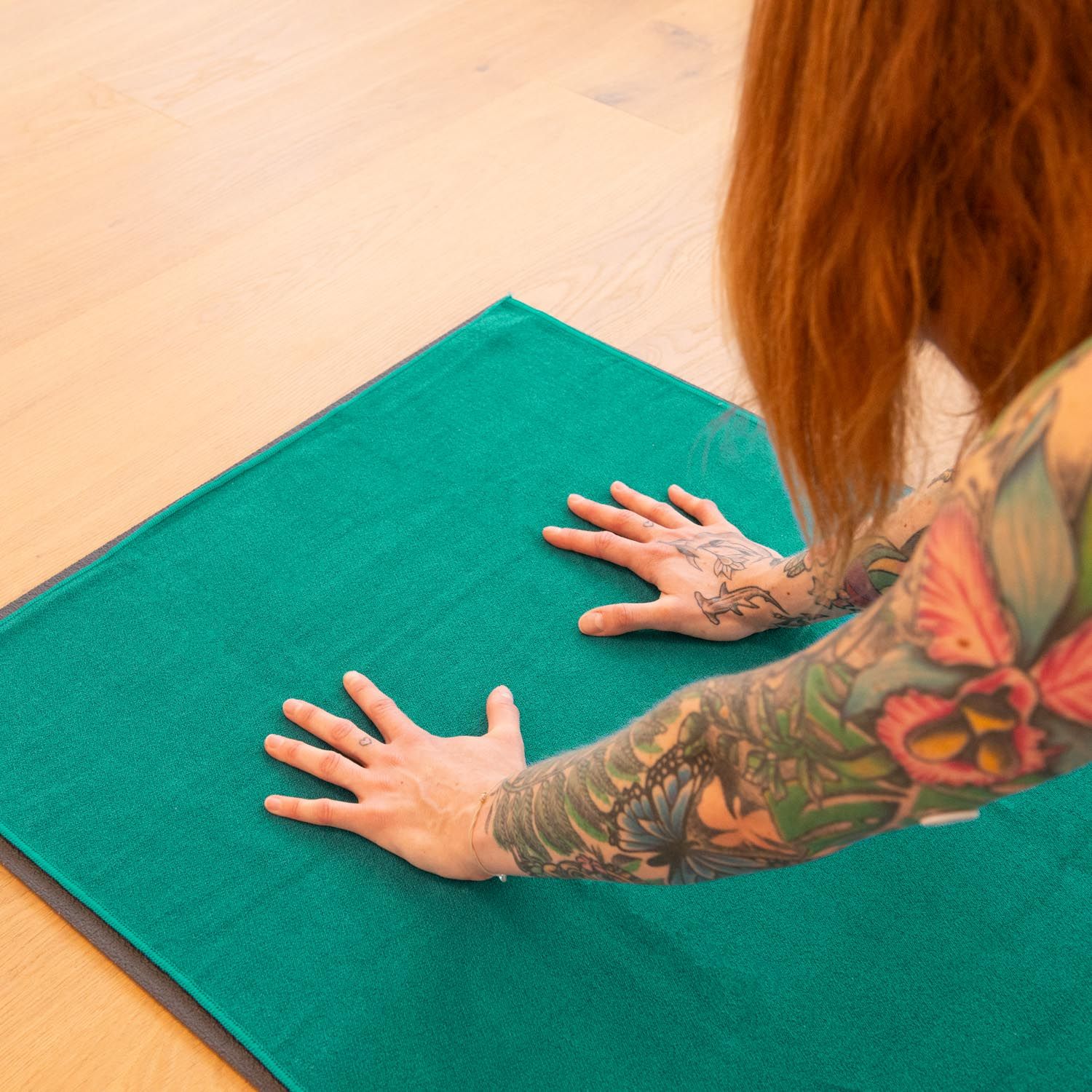 Person mit Tätowierungen auf grünem Yogahandtuch. Hände auf dem Handtuch.