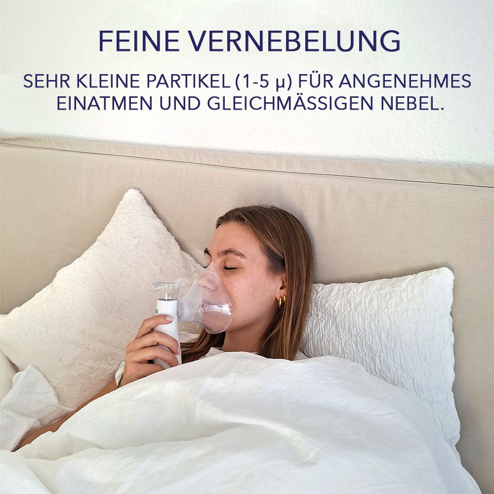 Frau liegt im Bett und benutzt ein weiß-rosa Inhalationsgerät mit Maske. Text: Feine Vernebelung, sehr kleine Partikel.